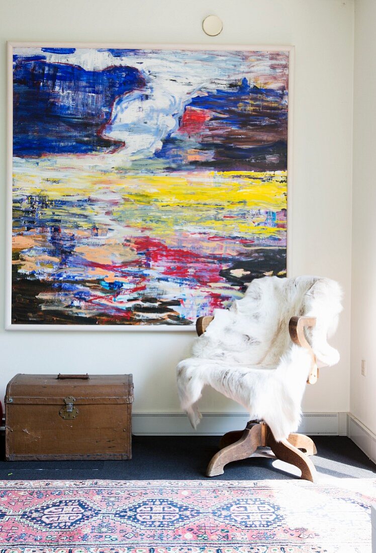 Fur blanket on old swivel chair and treasure chest below abstract artwork on wall