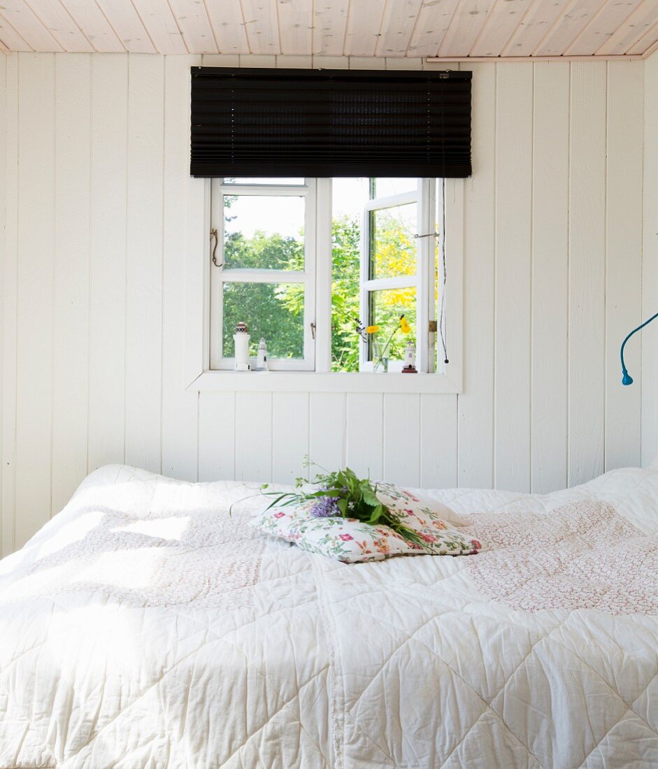 Small white bedroom with window opening onto summer garden