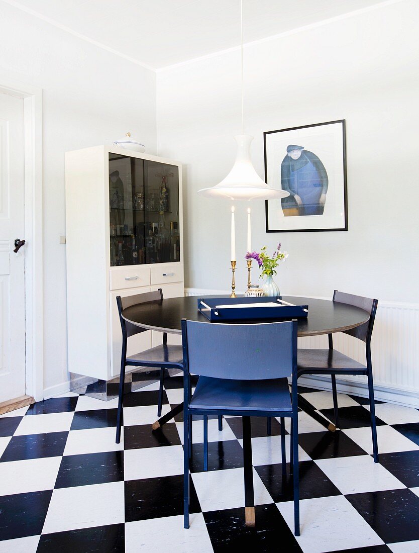 Round black table and blue chairs on black and white chequered floor