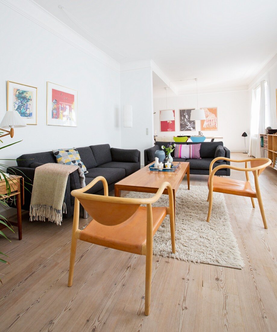 Wooden floor, black sofas and wood and leather chairs in open-plan interior of renovated period apartment