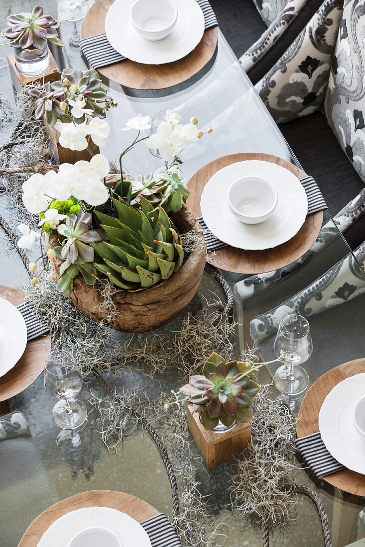 Table elegantly set with white china on wooden chargers and plant arrangement