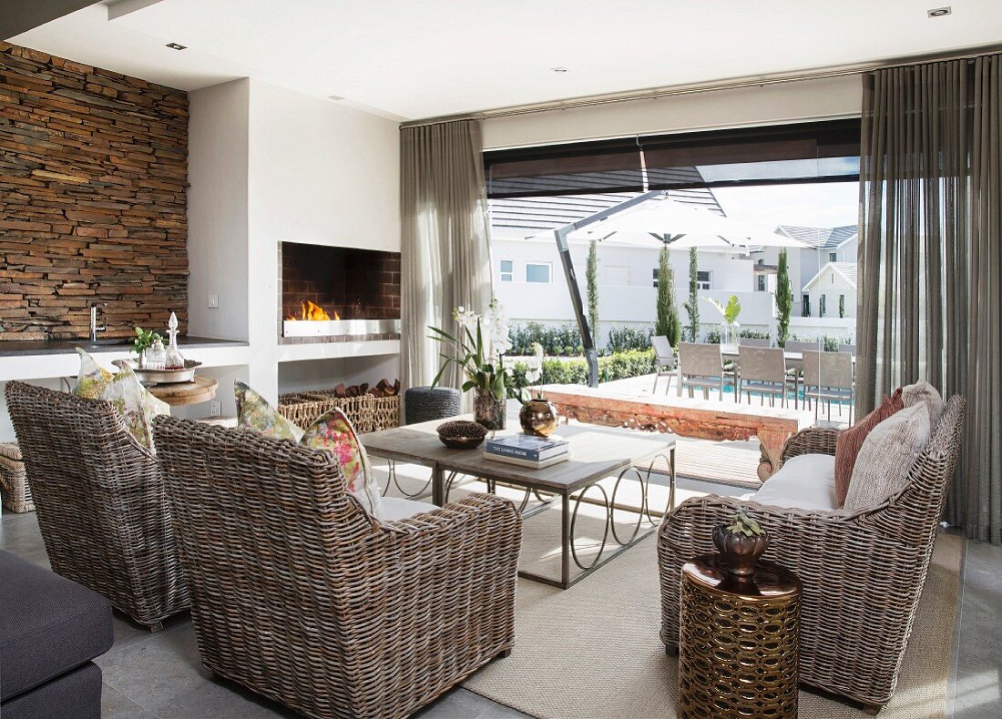 Lounge mit Korbmöbeln, Kaminfeuer und rustikaler Steinwand, Blick auf offene Terrasse