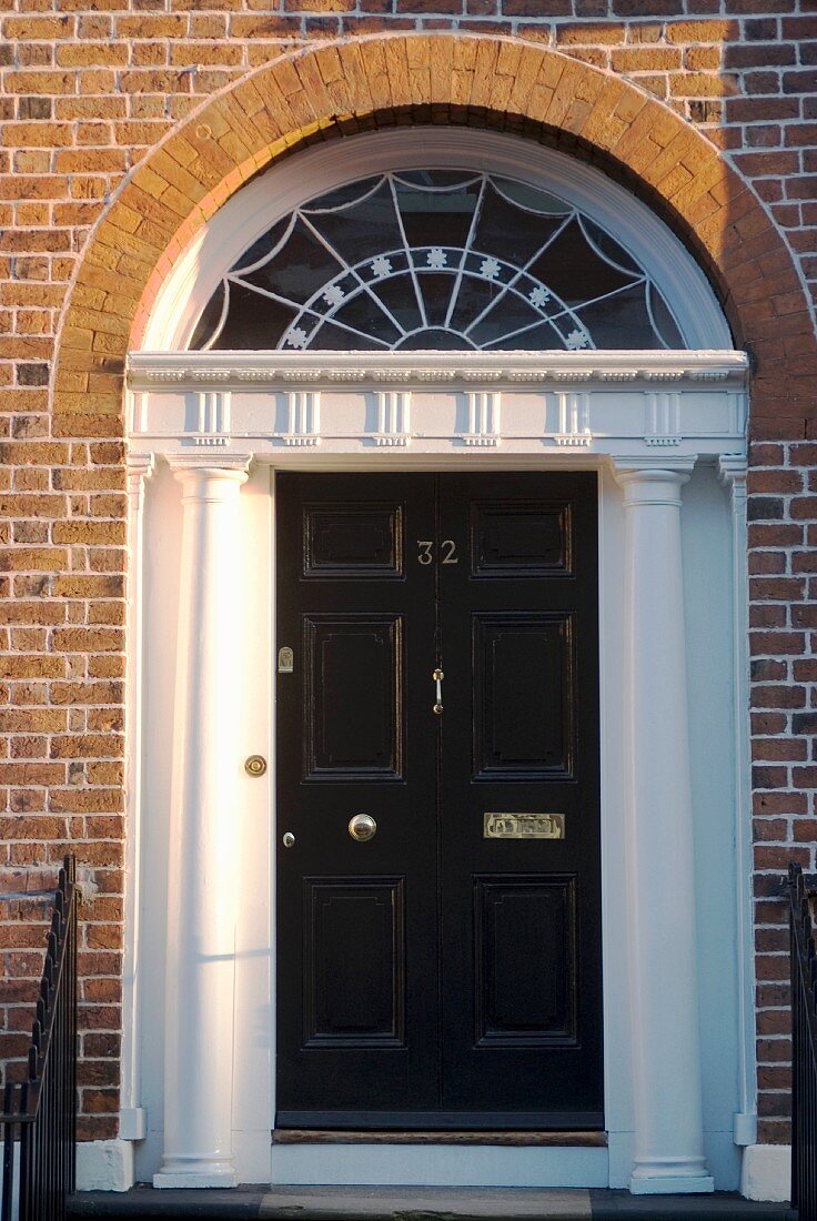 Klassischer Eingang mit schwarzer Haustür, Säulen und Bogenfenster