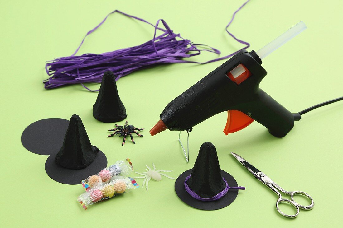 Bastelutensilien für Halloween-Dekoration; Klebepistole mit gebastelten 'Hexenhütchen', Süßigkeiten und Gummispinnen