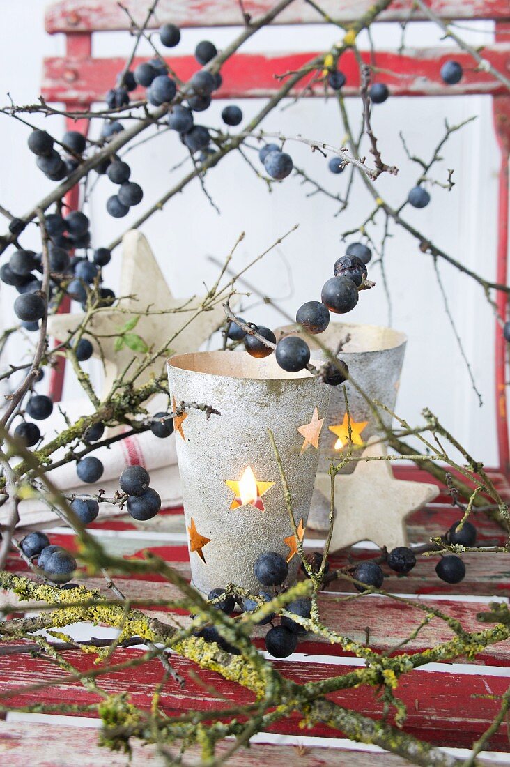 Candle lantern with punched stars amongst sloe branches on red chair