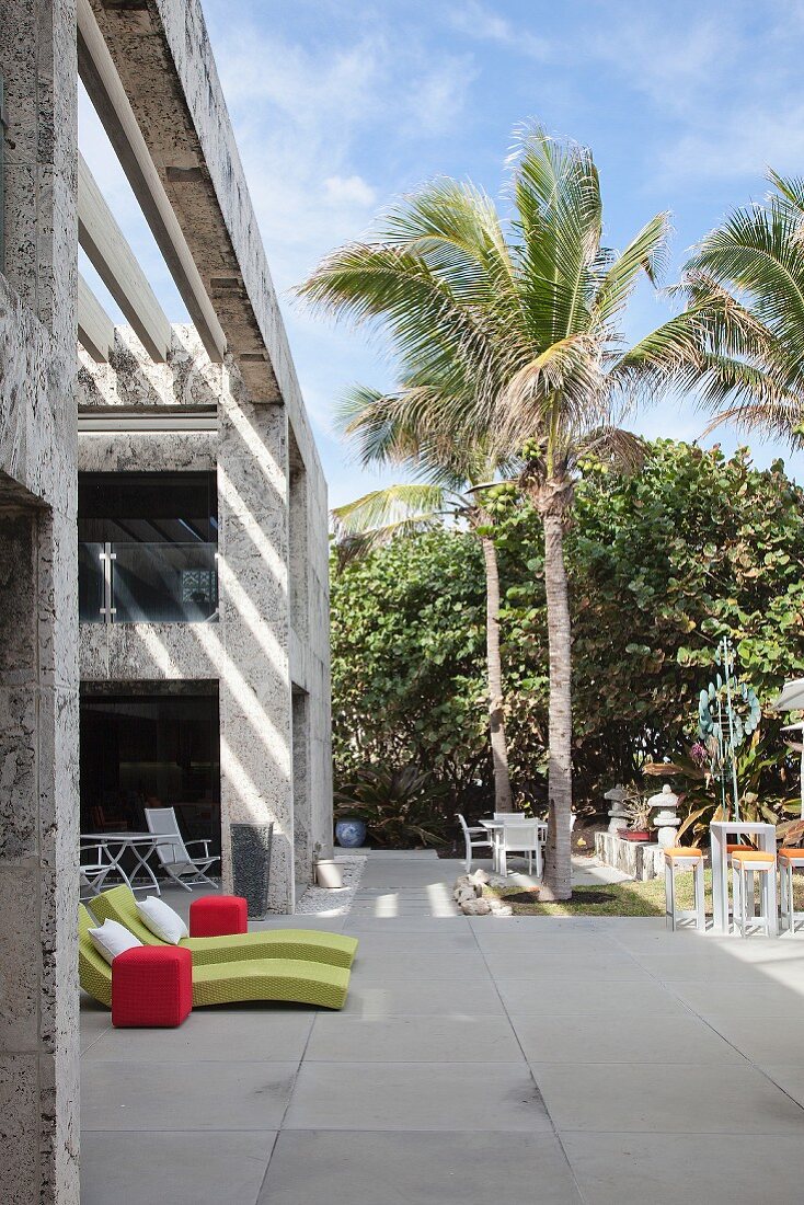 Liegen und Sitzplätze auf moderner Terrasse unter Palmen