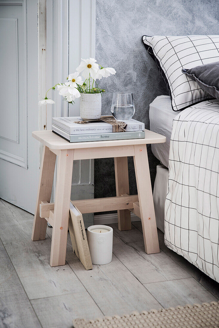 Wooden stool as a bedside table in the bedroom in shades of gray