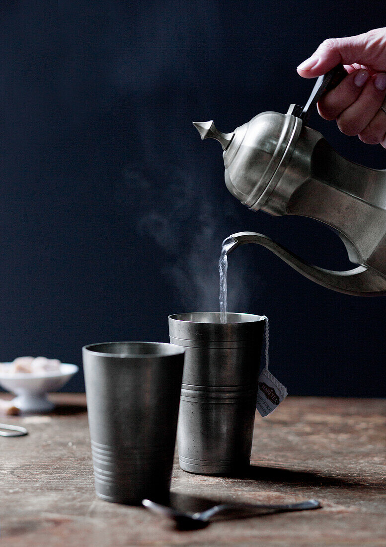 Hot water being poured from pot into pewter beakers