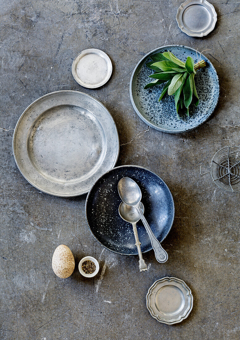 Various plates and pewter spoons on concrete floor