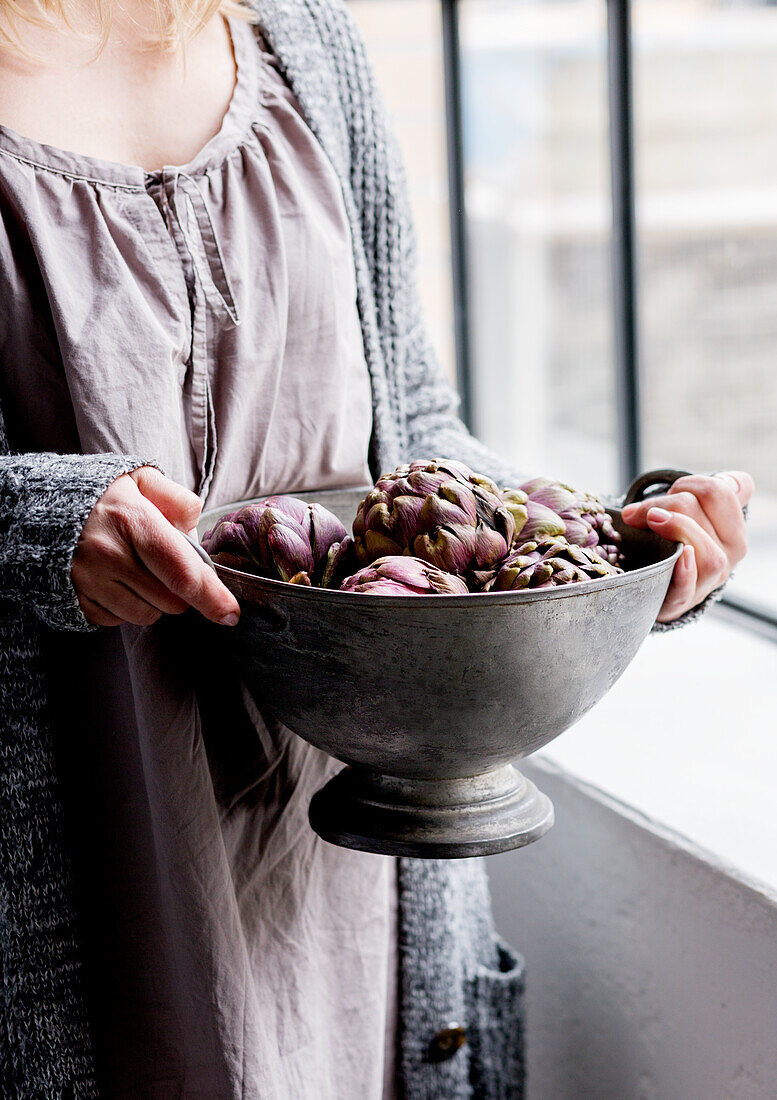 Woman carrying pewter bowl of artichokes