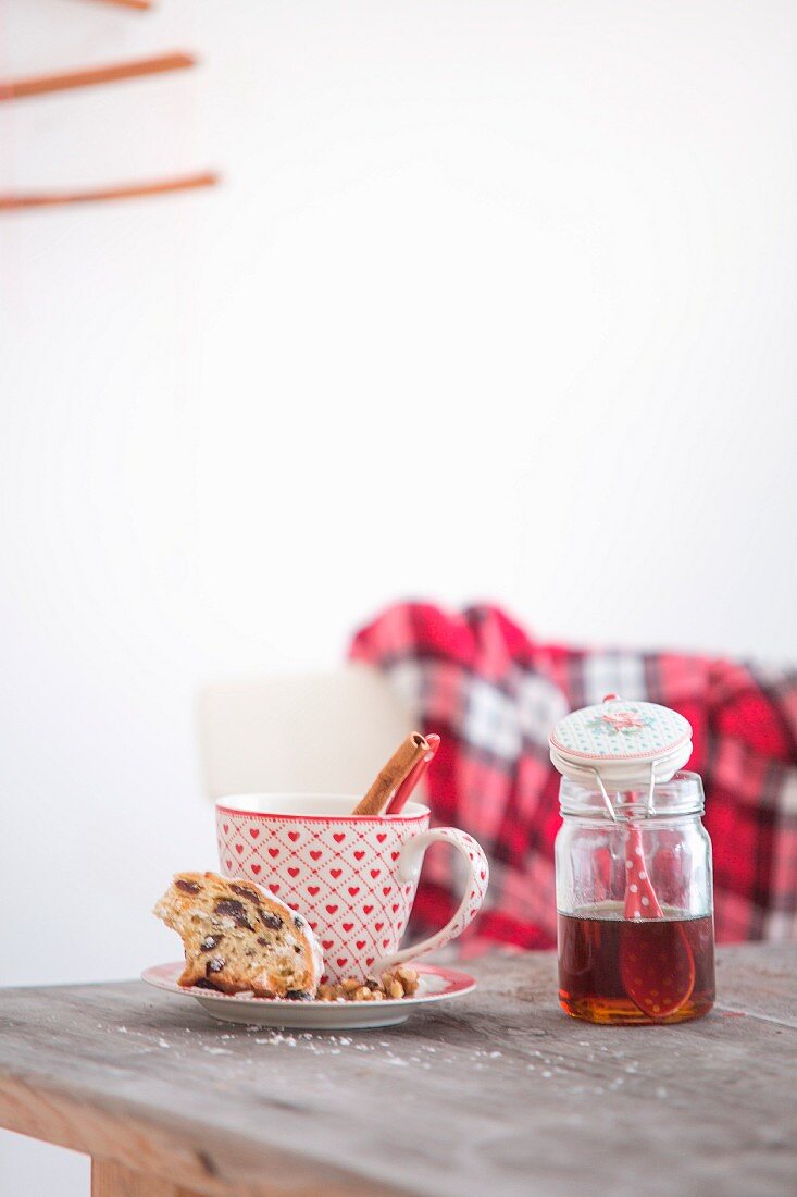 Christstollen, rot-weiße Tasse mit Zimtstange und Honigglas auf Holztisch