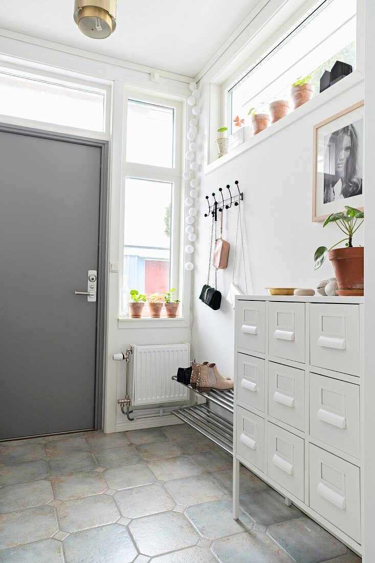 White chest of drawers, coat pegs and grey front door in bright hallway