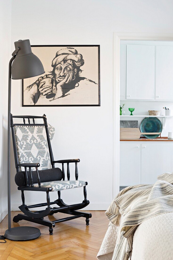 Black wooden rocking chair next to standard lamp and below black-framed drawing on wall