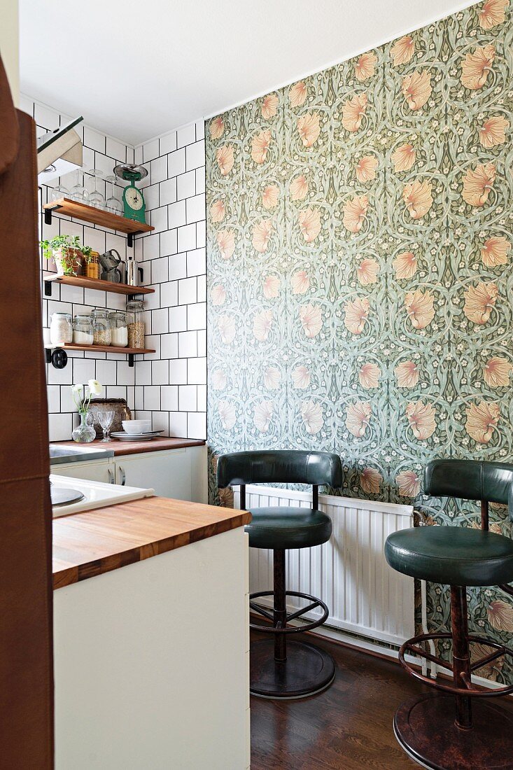 Dark green retro bar stools against floral wallpaper in kitchen
