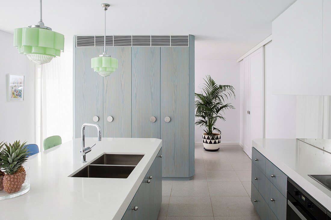 Schlichte Küche in Weiß-Graublau mit Fliesenboden, Kücheninsel und pastellgrünen Deckenleuchten