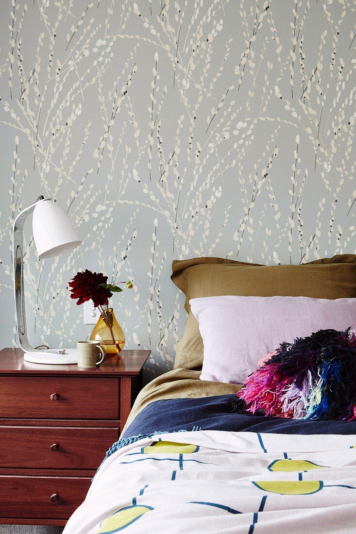 Bett mit verschiedenen Textilien vor floral gemusterter Wand