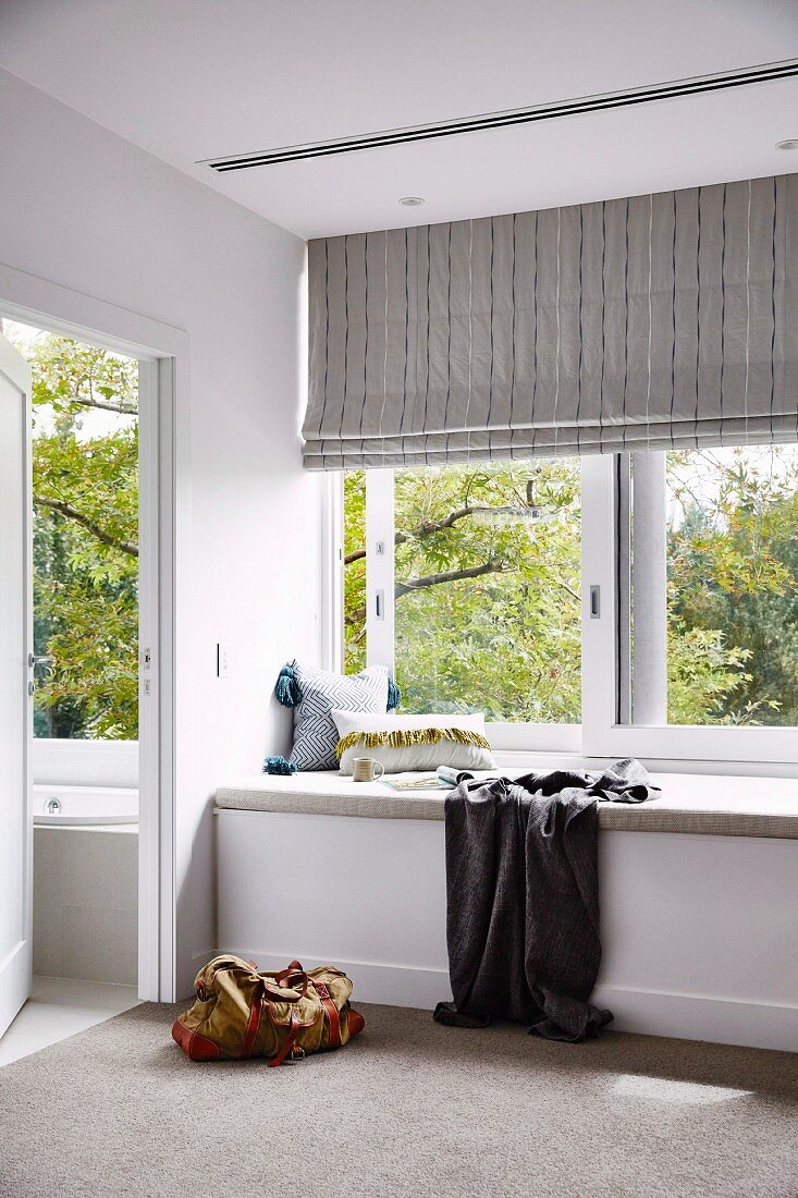 Upholstered bench in front of the window with a striped roller blind