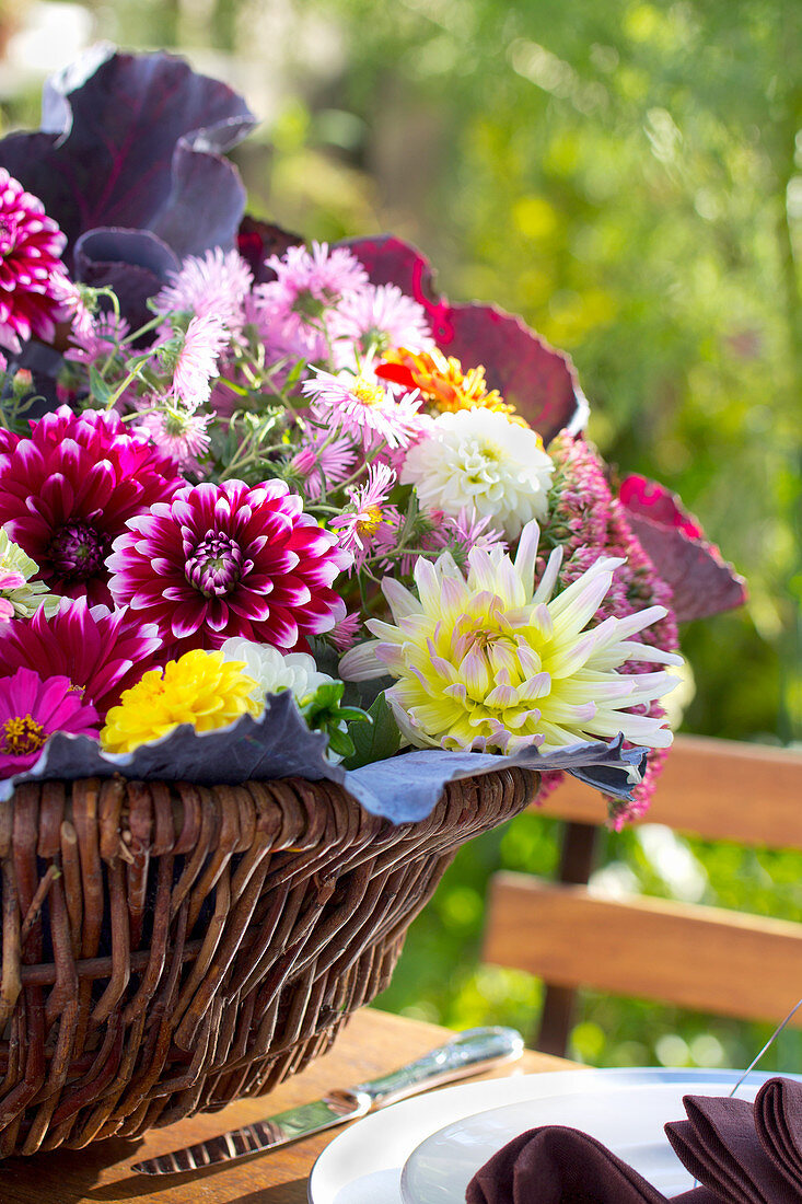 Korb mit Herbststrauß aus Kohlblättern, Hortensienblüten Astern und Dahlien