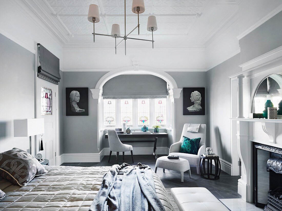 Elegant bedroom in gray tones with double bed, fireplace, upholstered armchair and table in front of the window