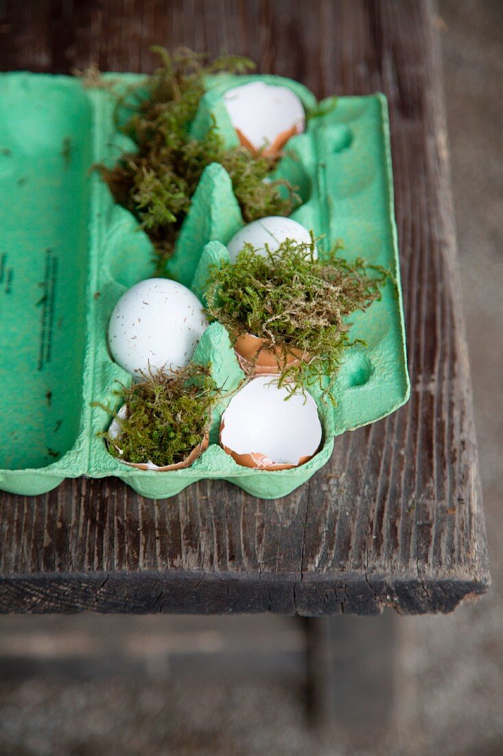 Osterdekoration mit grüner Eierschachtel, Moos und Eierschalen auf Holztisch