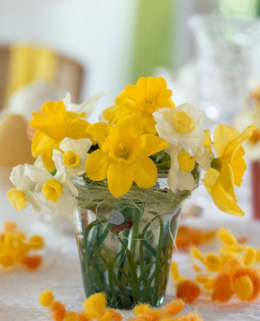 Small daffodils bouquet in glass vase with grass and bees decor