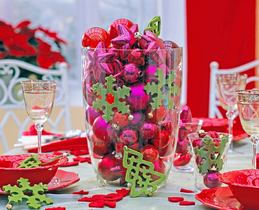 Roter und pinker Baumschmuck in großer Glasvase, grüne Filzanhänger