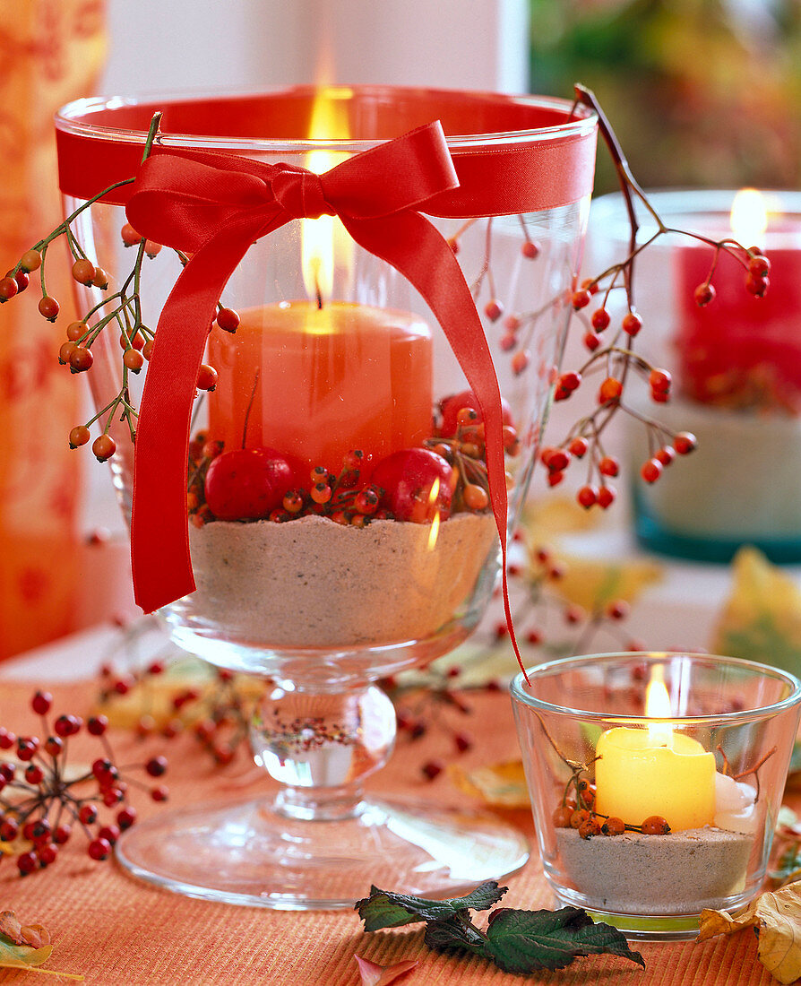 Rosa (Hagebutten), Malus (Zierapfel), Glaspokal mit Sand, orange Kerze