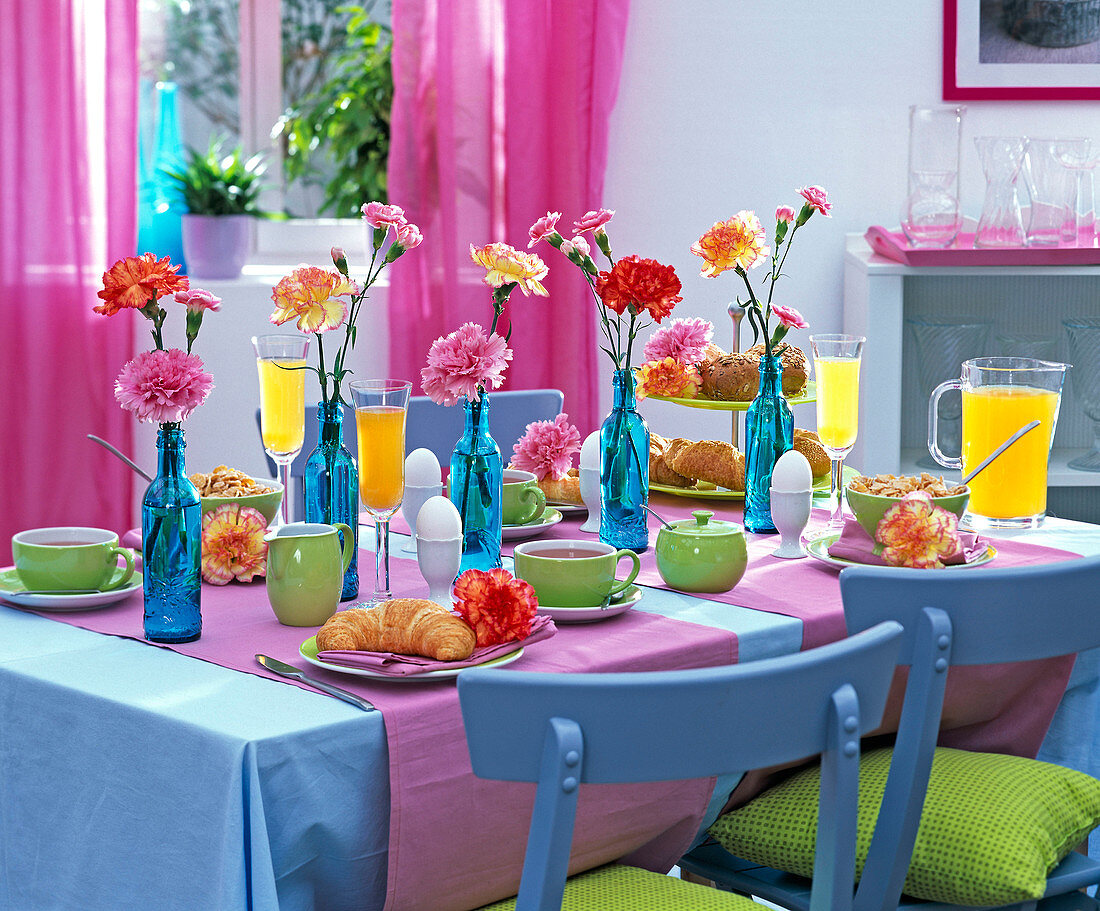 Breakfast table with dianthus in blue bottles, orange juice