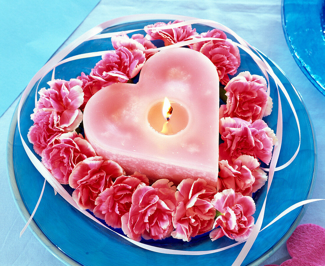 Dianthus flowers, placed around pink candle in heart shape