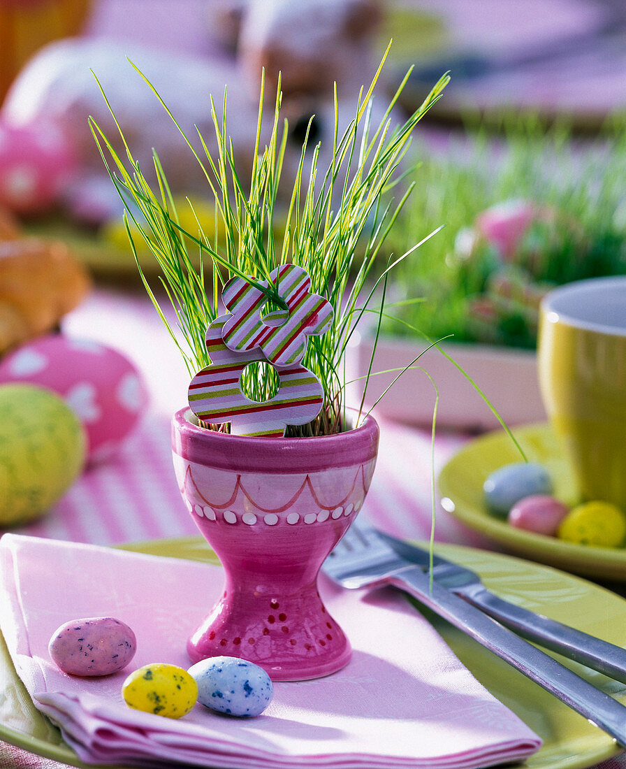 Easter grass seeded in pink egg cups, wood flowers, sugar eggs, napkin