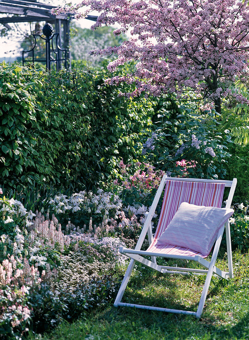White bed in front of hedge, folding chair