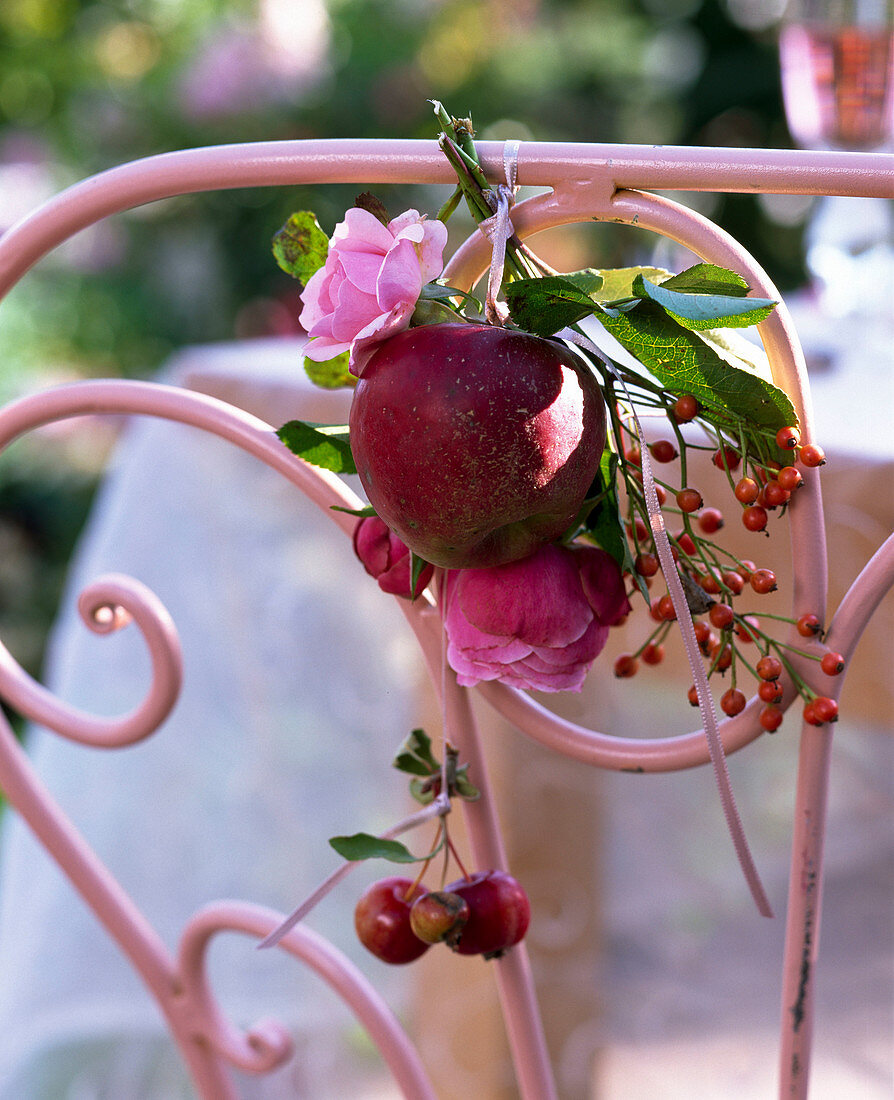 Kleiner Strauß aus Rosa (Rosen, Hagebutten) und Malus (rotem Apfel) an Stuhl