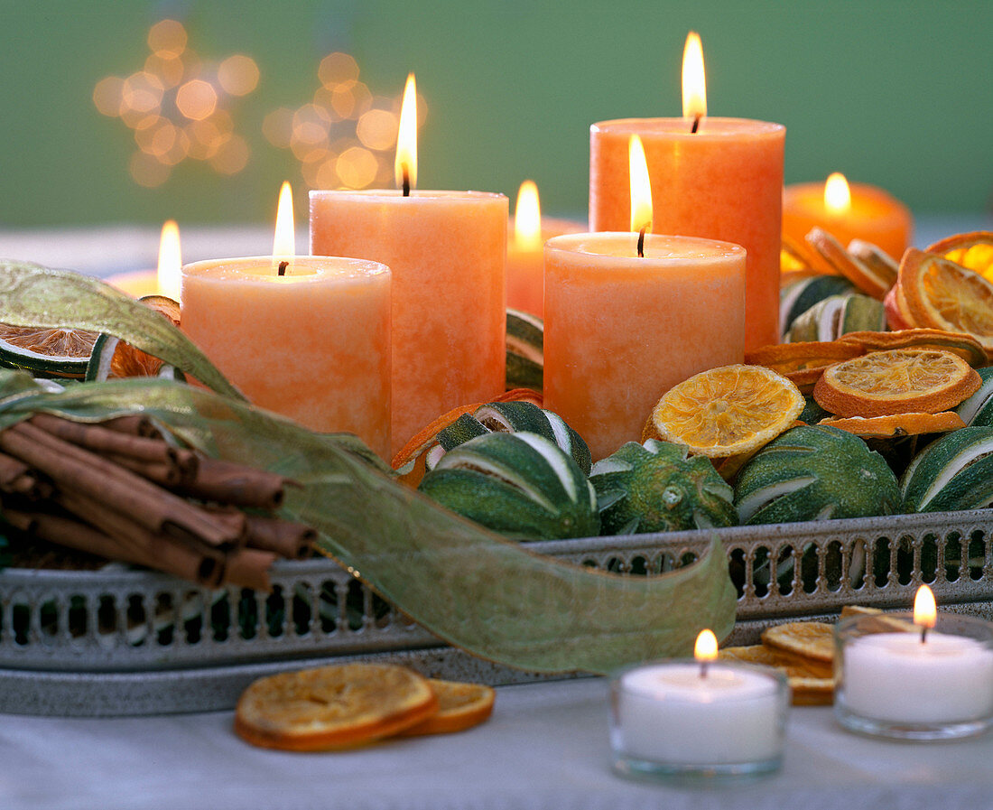 Orange Kerzen, Citrus (Limetten, Orangenscheiben) und Zimtstangen auf Tablett