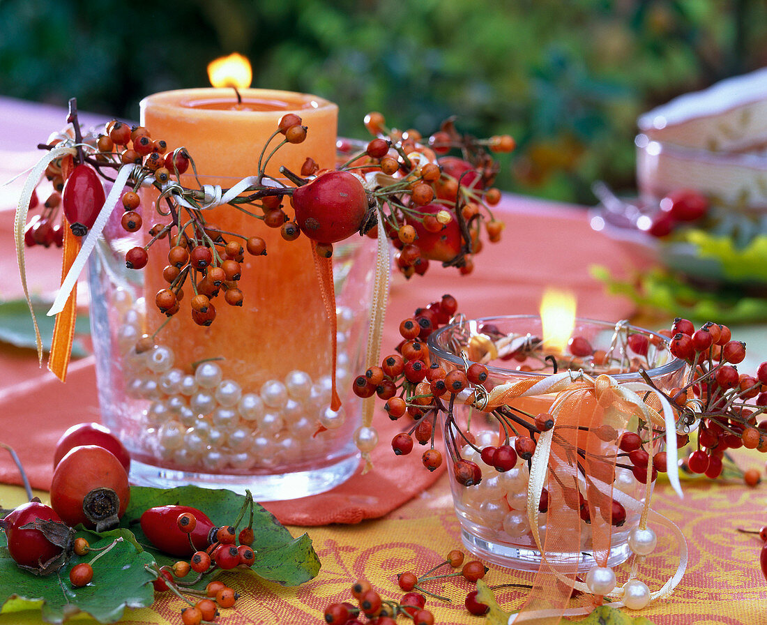 Rosa (Hagebutten) an mit Perlen gefüllten Gläsern mit orangen Kerzen