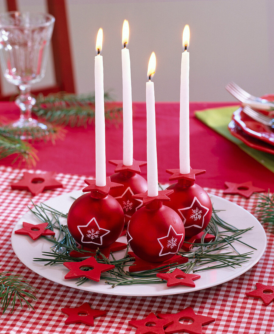 Adventskranz aus roten Weihnachtsbaumkugeln mit Sternmotiven und weißen Kerzen