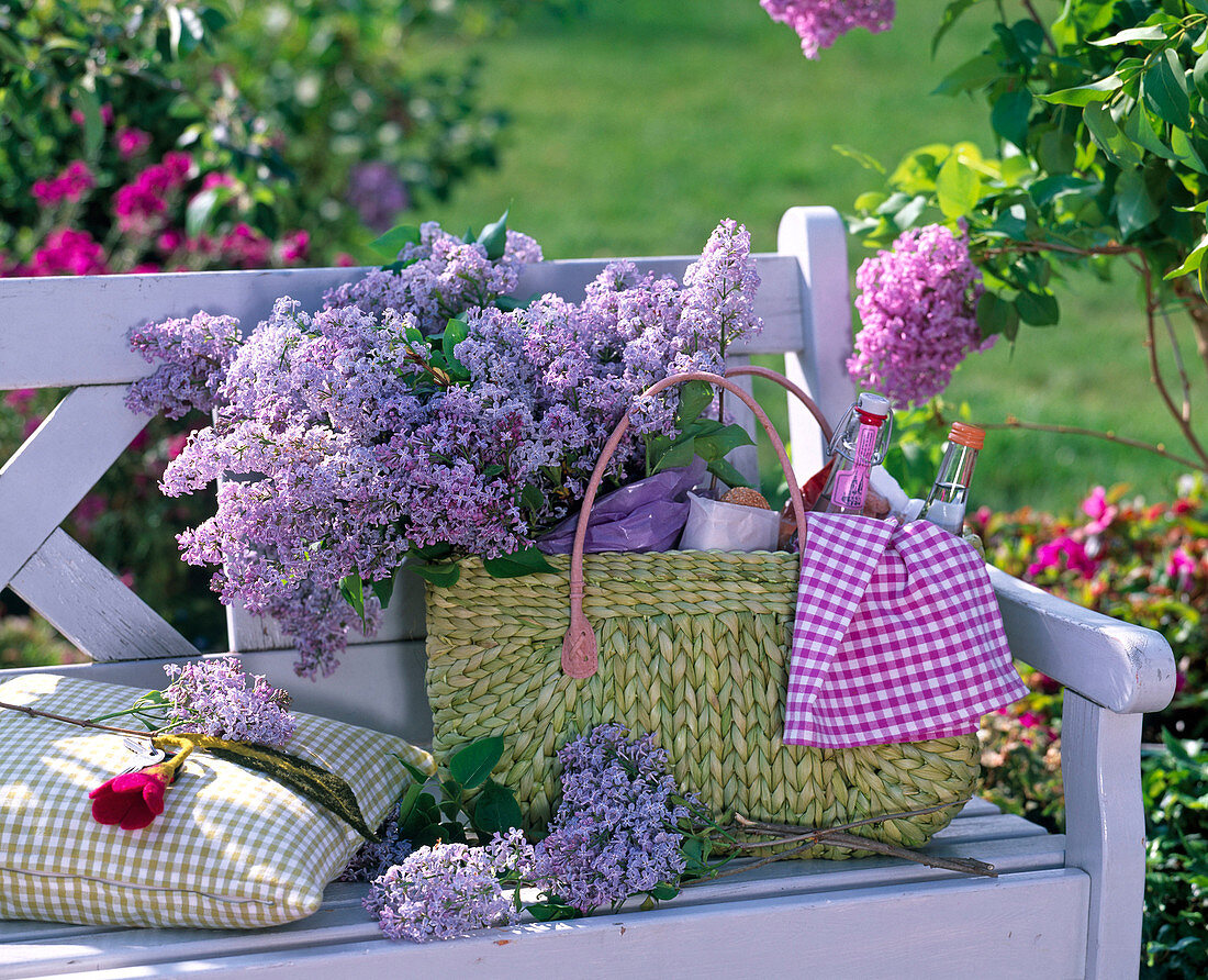 Syringa in wicker bag with bottles, bread, towel on white bench