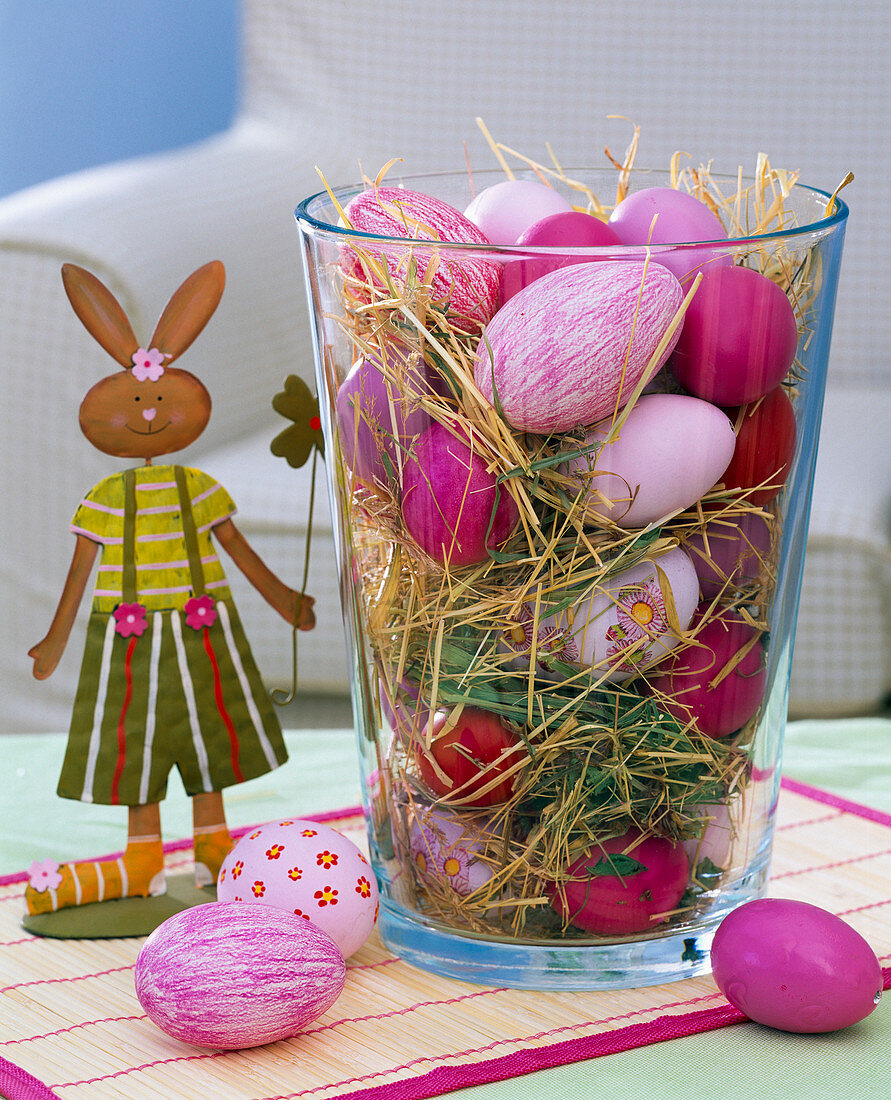 Blown pink easter eggs in glass vase with straw, bamboo coaster, bunny