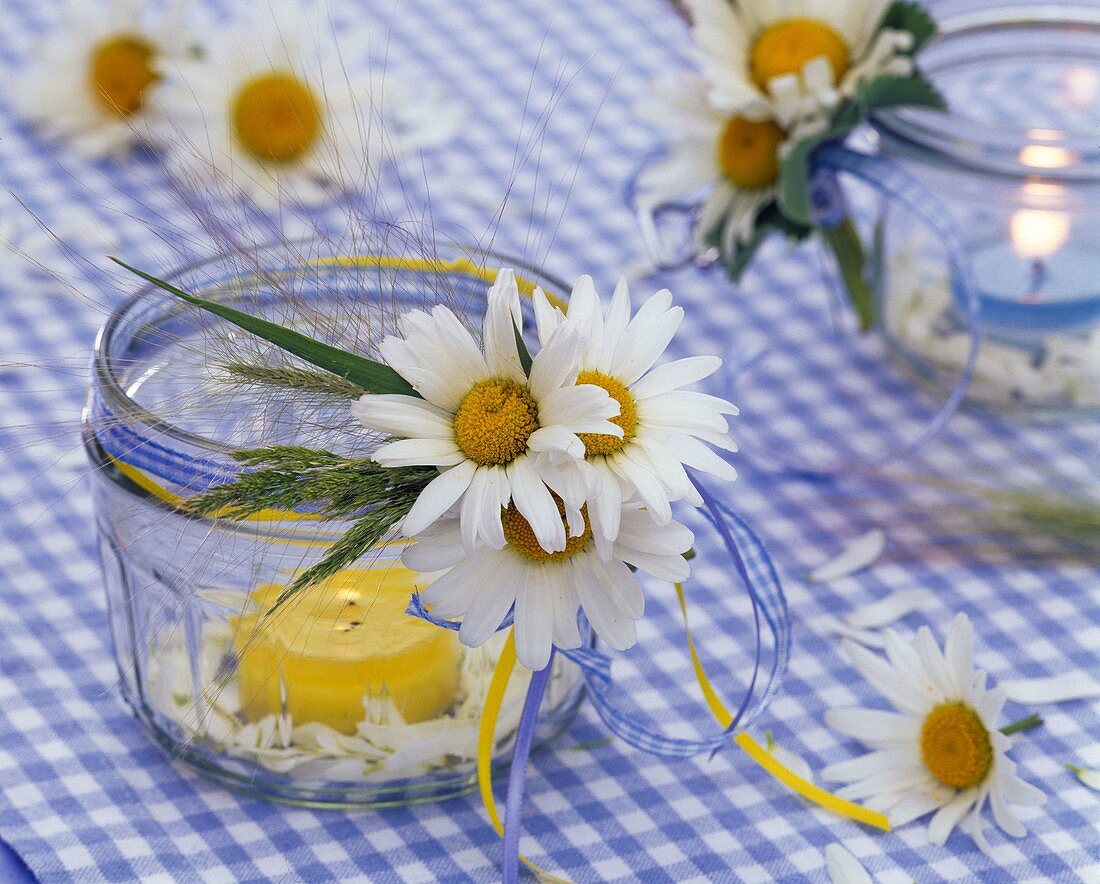 Leucanthemum (Margeriten) und Gräser an Einmachglas mit gelber Kerze