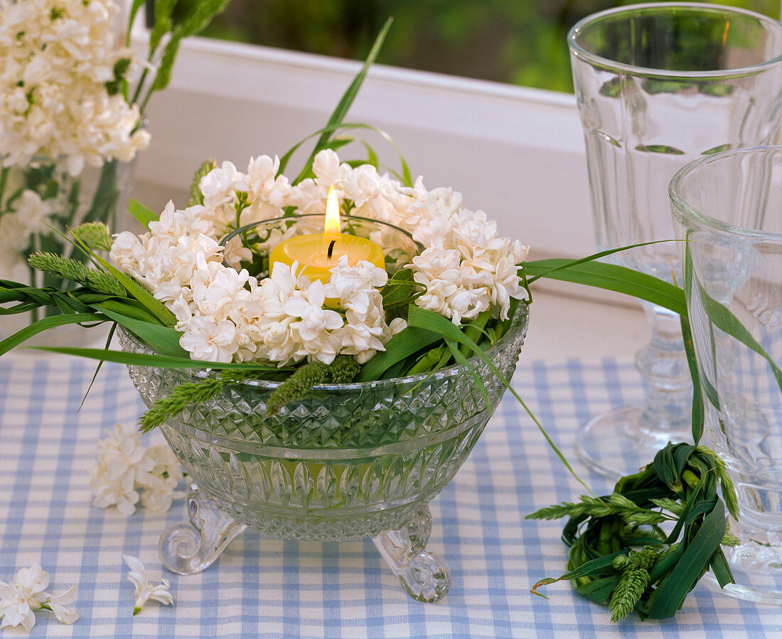 Windlicht mit Syringa (Flieder) und Kranz aus Gräsern in Glasschale