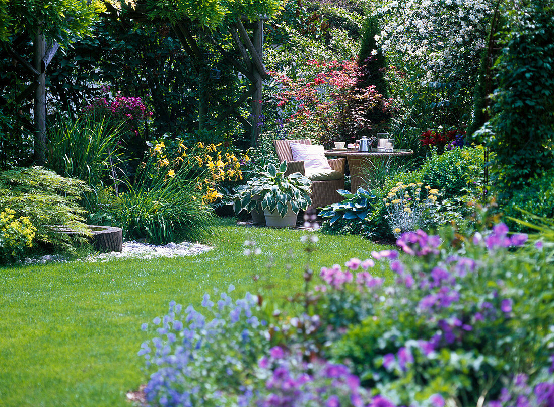 Gartenansicht mit Blick auf kleine Terrasse mit Sitzplatz, bewachsene Pergola