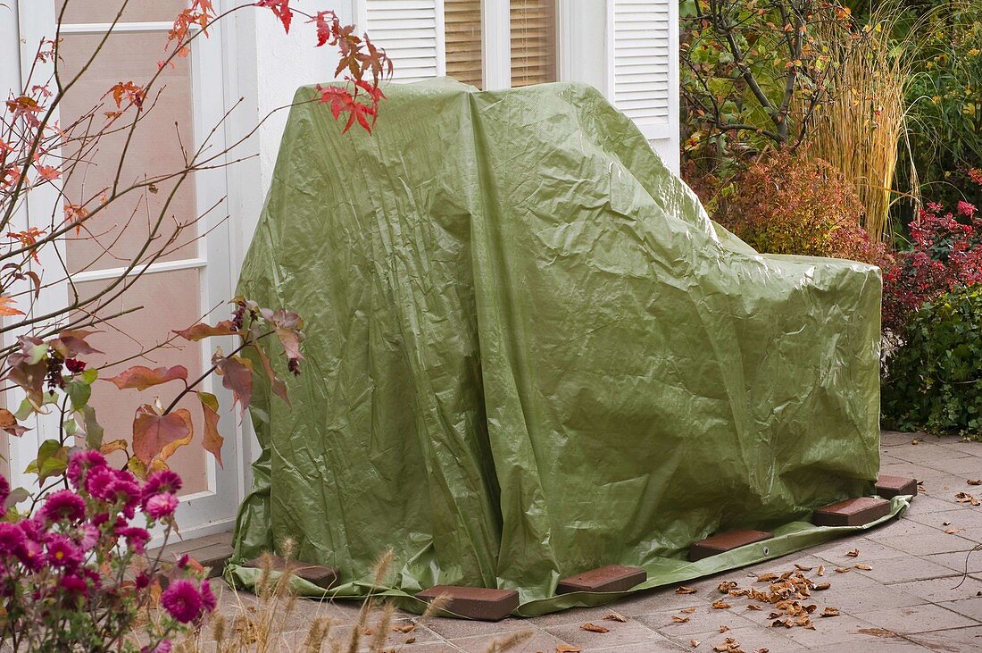 Garden furniture in the fall with green tarp wintering