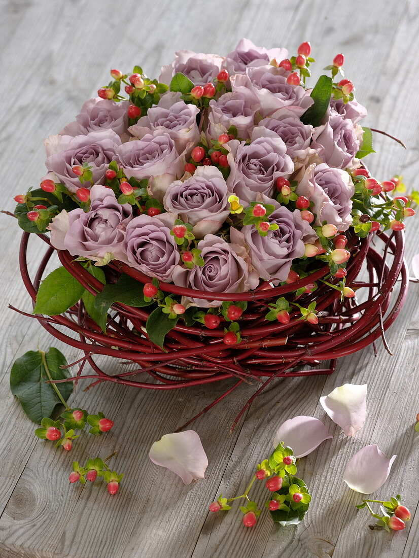 Gesteck aus lila Rosen und Johanniskrautfrüchten in Kranz aus Hartriegelzweigen