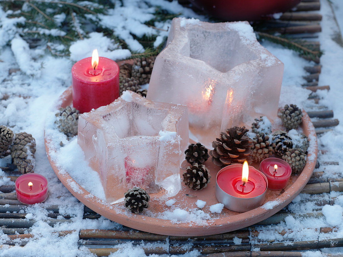 Windlichter - Eissterne auf Terracotta - Untersetzer mit Zapfen und roten Kerzen