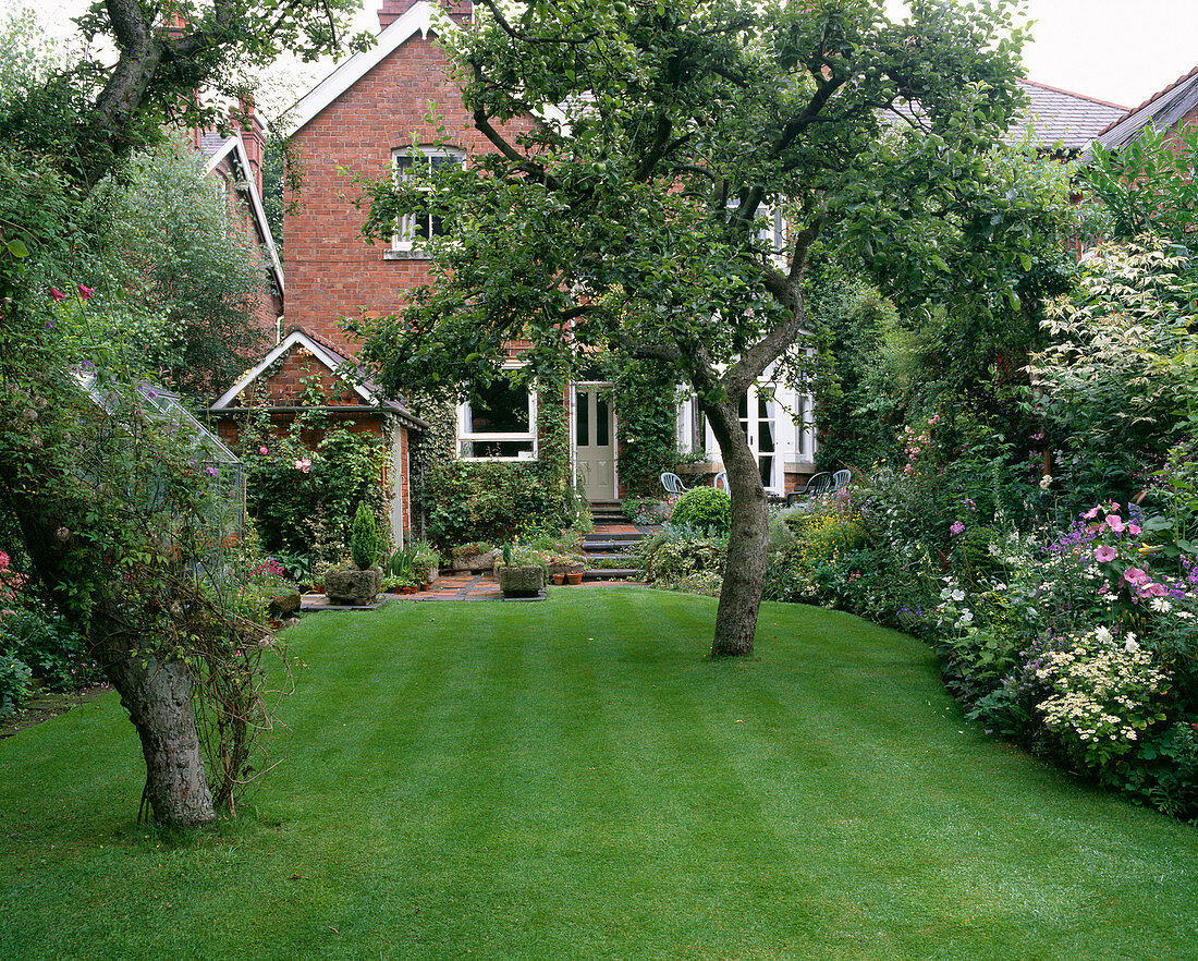 Gepflegter Rasen und Terrasse auf der Rückseite des Hauses mit alpinen Trögen