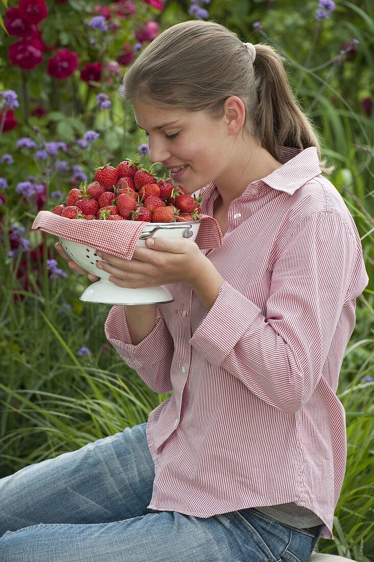 Junge Frau genießt den Duft von frisch gepflückten Erdbeeren (Fragaria)