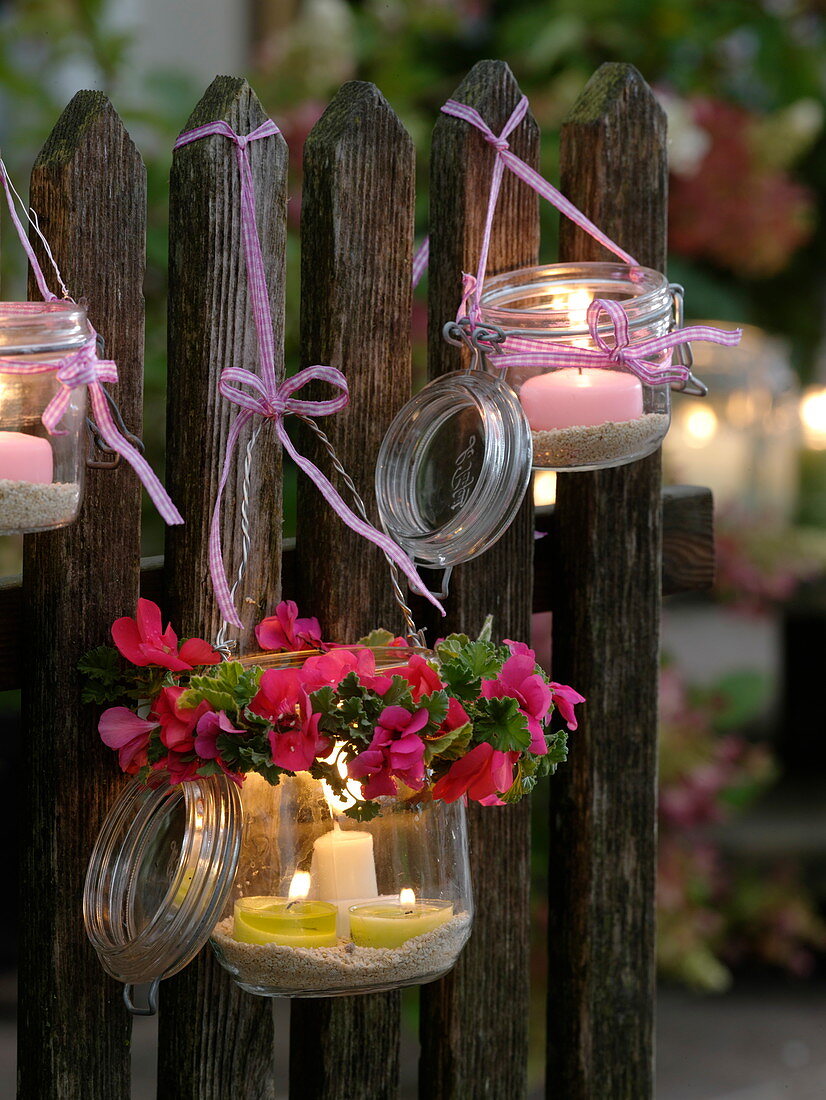 Deckelgläser als Windlichter an Zaun gebunden, Kranz aus Pelargonium