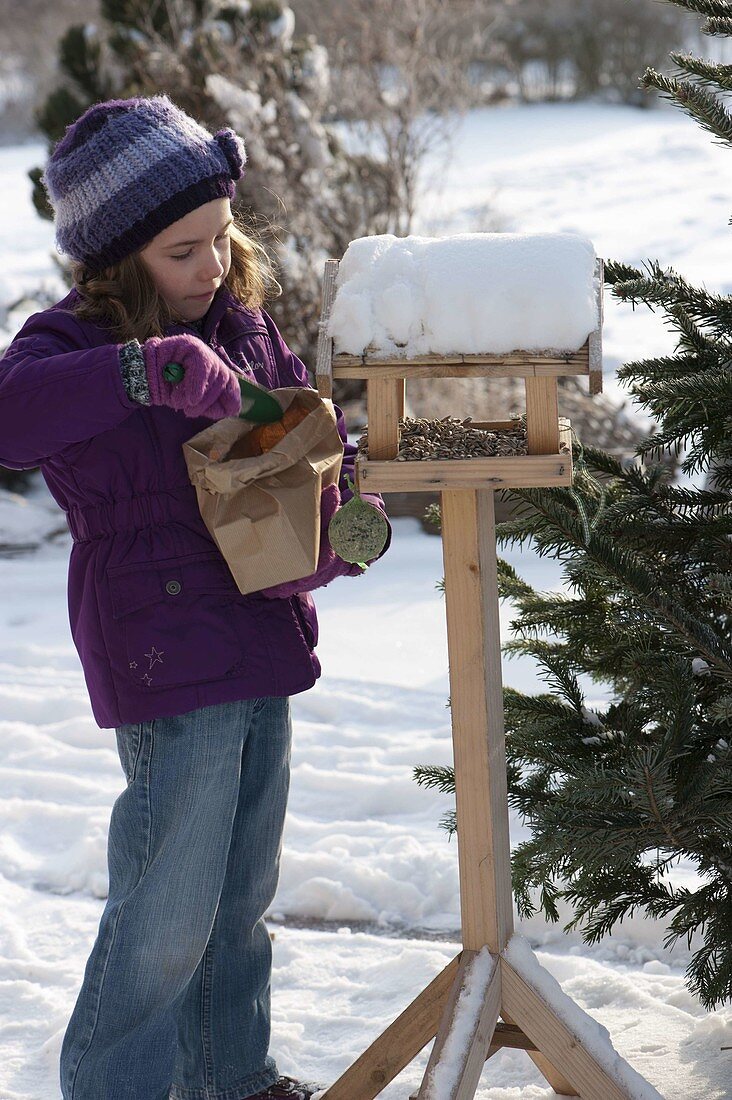 Girl filling birdhouse with sunflower seeds