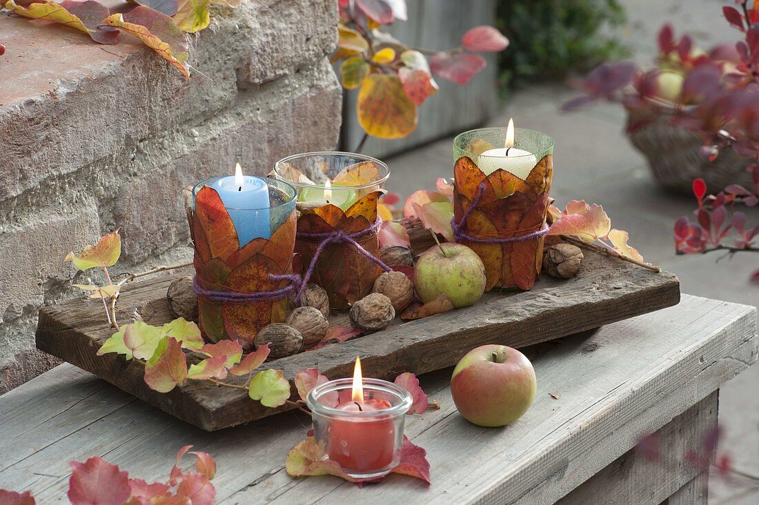 Kleine Windlichter mit Blättern umwickelt, Äpfel (Malus) und Walnuessen