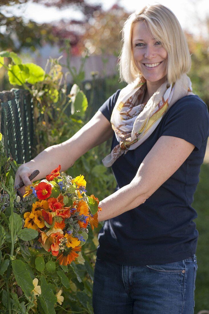 Frau pflückt Strauss von Sommerblumen mit essbaren Blüten