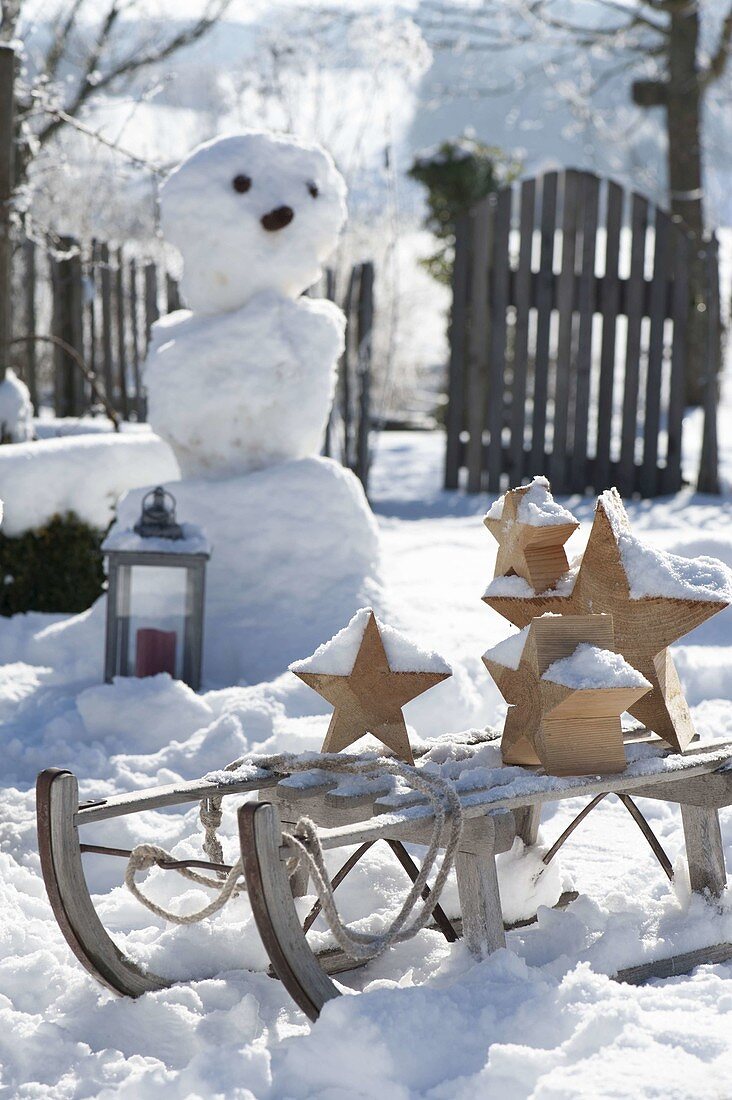 Verschneiter Garten mit Schneemann und Schlitten mit Holz-Sternen